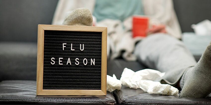 sign says "flu season" with sick person sitting behind it