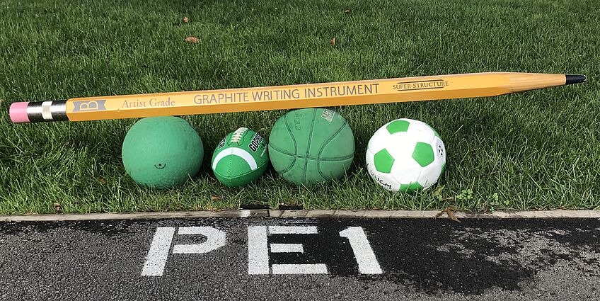 giant pencil on top of some sport balls