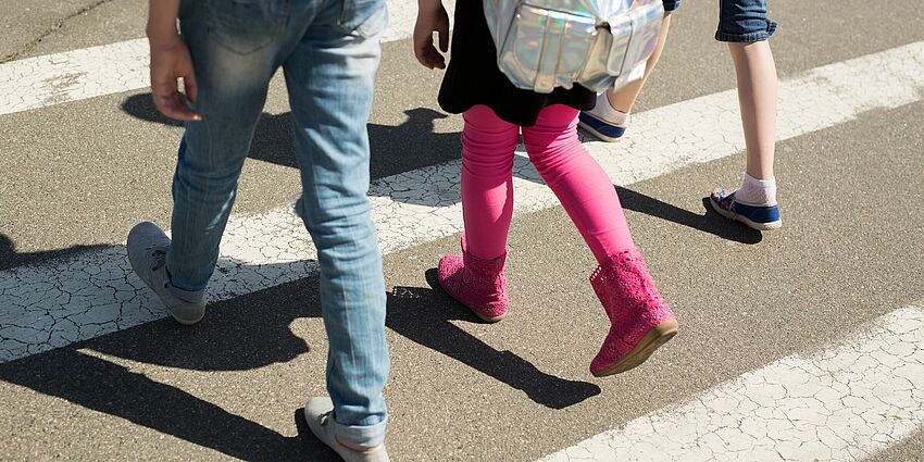 feet and legs of three children walking in the crosswalk of a street