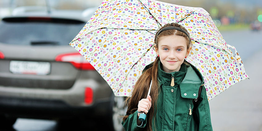 smiling girl holding umbrella as car drives away