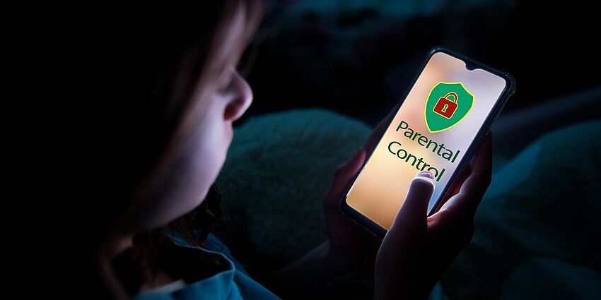 young child in a dark room looking at a lighted smartphone screen that says 