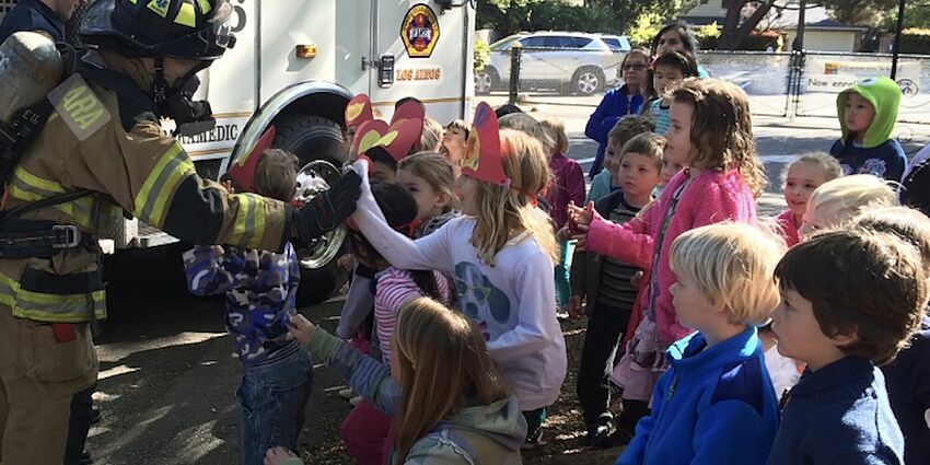 children gather around a firefighter as he shows them the fire truck