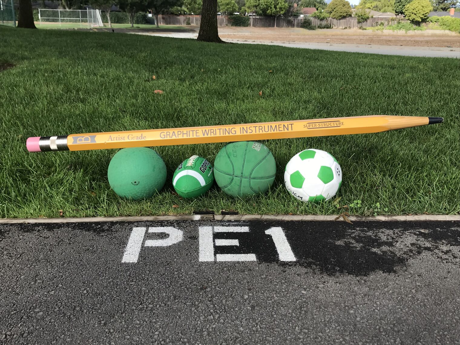 giant pencil on top of some sport balls