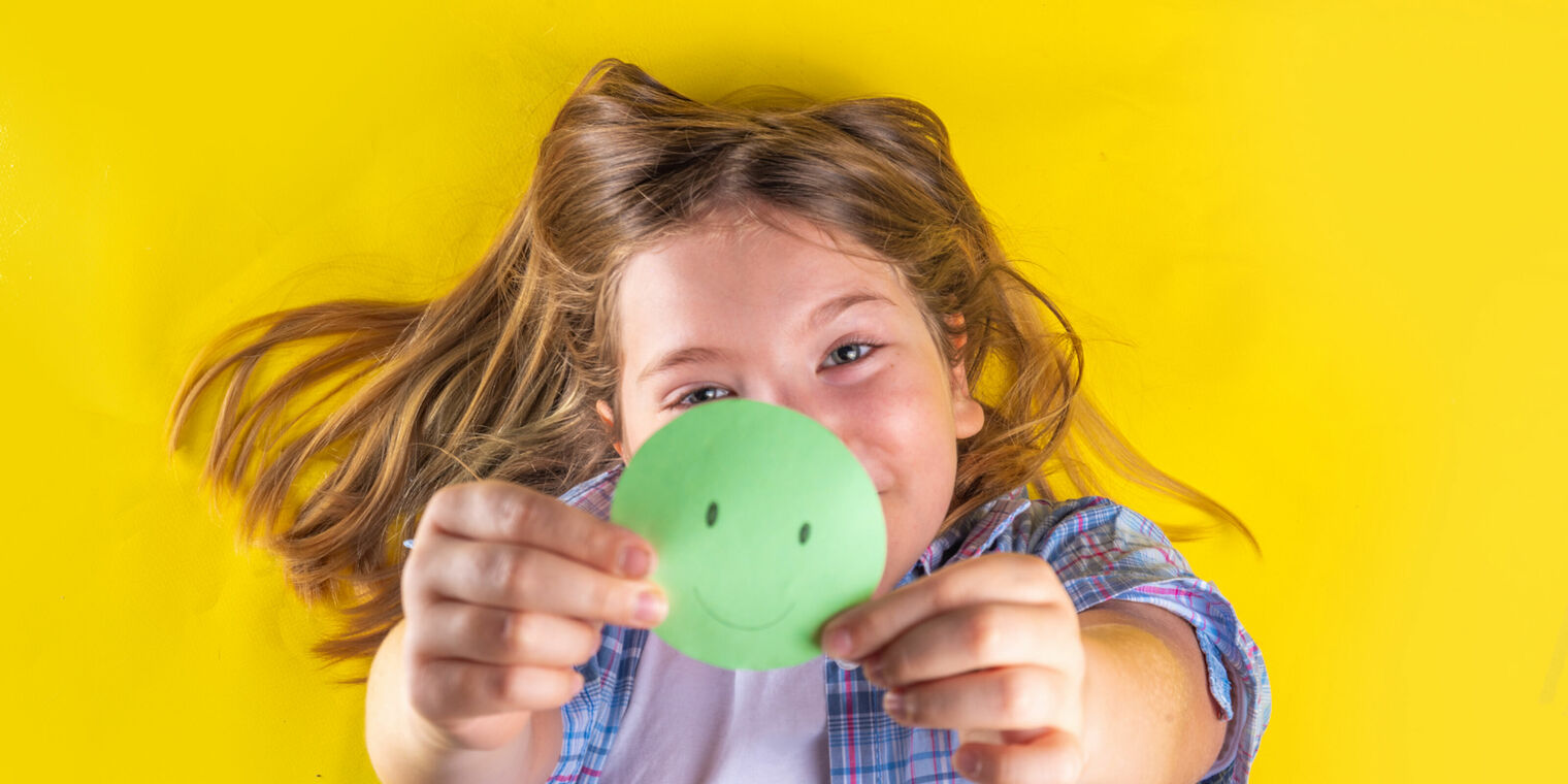 smiling young girl holding a green circle with a happy face drawn on it.